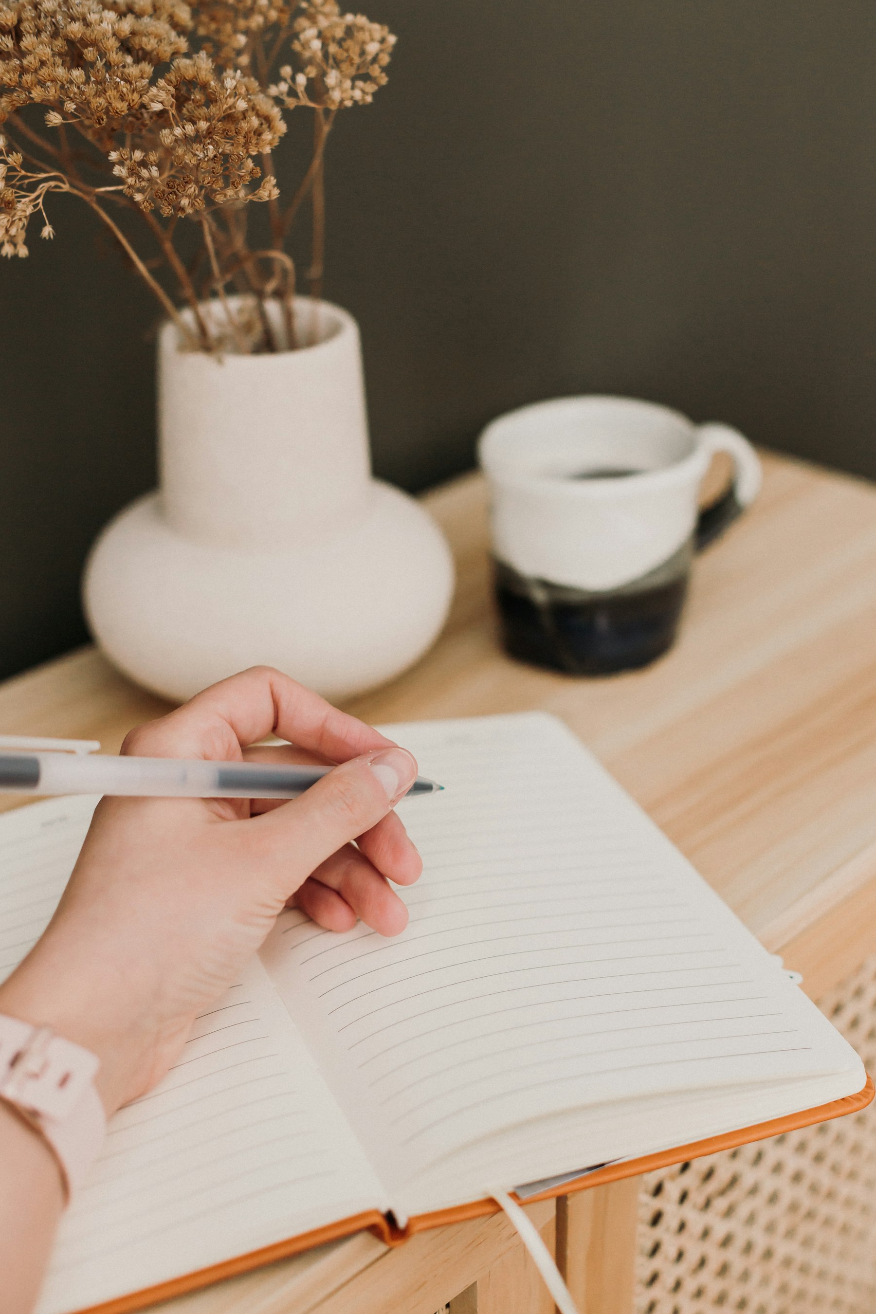 Une main écrit dans un carnet au petit matin, tasse posée à côté