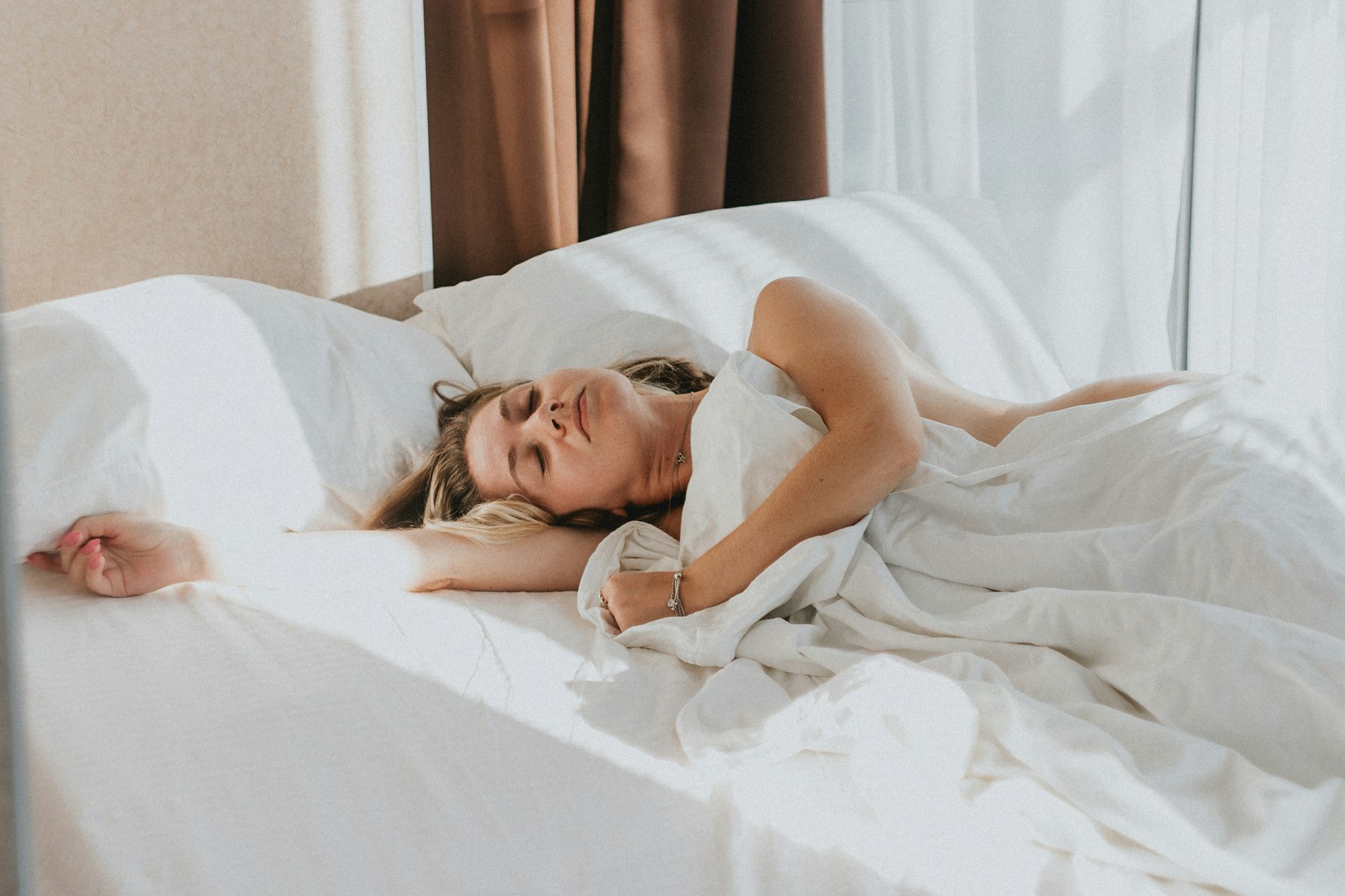 Une femme s'étire au réveil dans un lit aux draps clairs